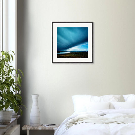 Framed artwork above a bed in a bedroom with a plant and side table.