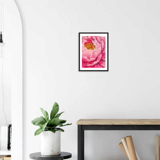 Framed pink floral artwork on a white wall above a wooden desk with a plant.