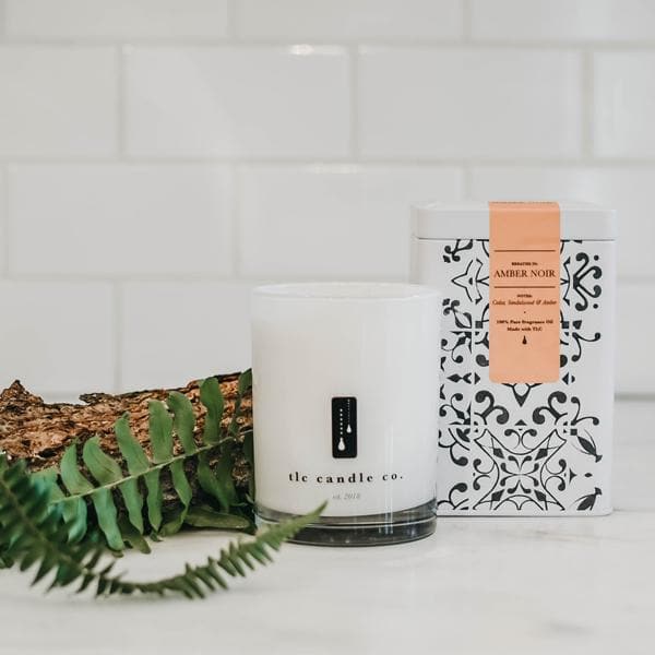 Amber Noir Sandalwood soy candle by DC-TLC Candle Co. in a glass jar with a lit wick, emitting a warm, amber and sandalwood fragrance.