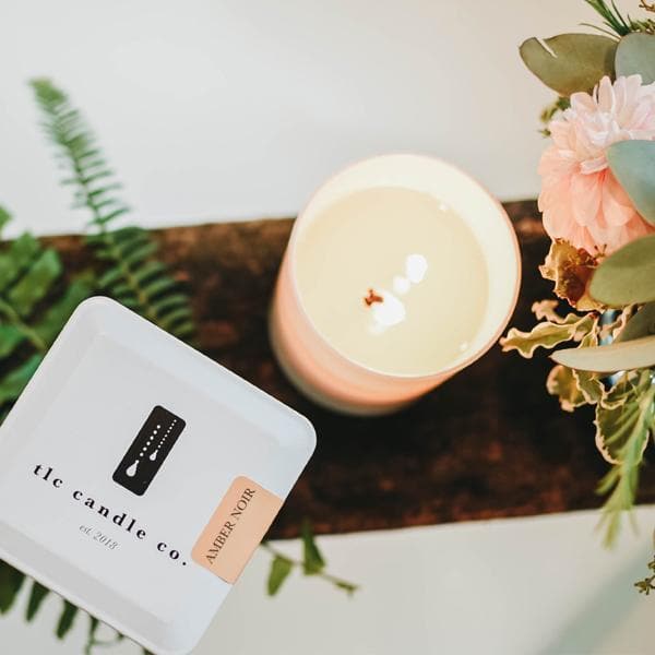 Amber Noir Sandalwood soy candle by DC-TLC Candle Co. in a glass jar with a lit wick and a warm, amber-colored wax.