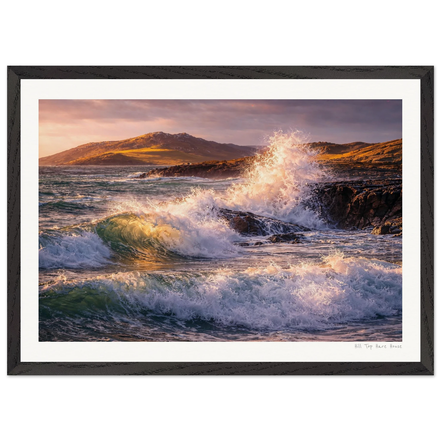 Framed artwork of waves crashing against a rocky shore with mountains in the background.