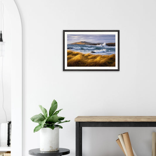 Framed landscape print on a wall above a desk with a plant