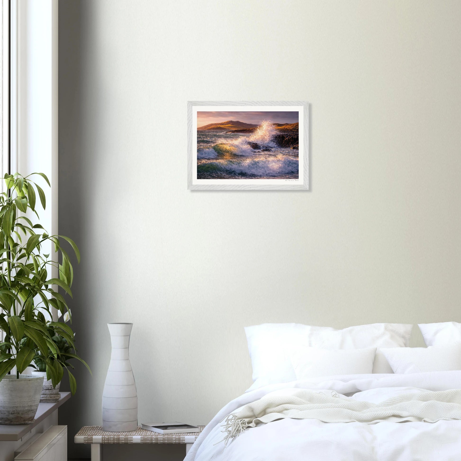 Framed artwork of a sunset over water hanging on a wall above a bed.