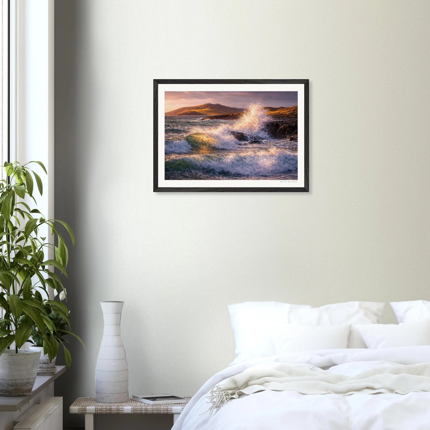Framed artwork of a sunset over water hanging on a wall above a bed.