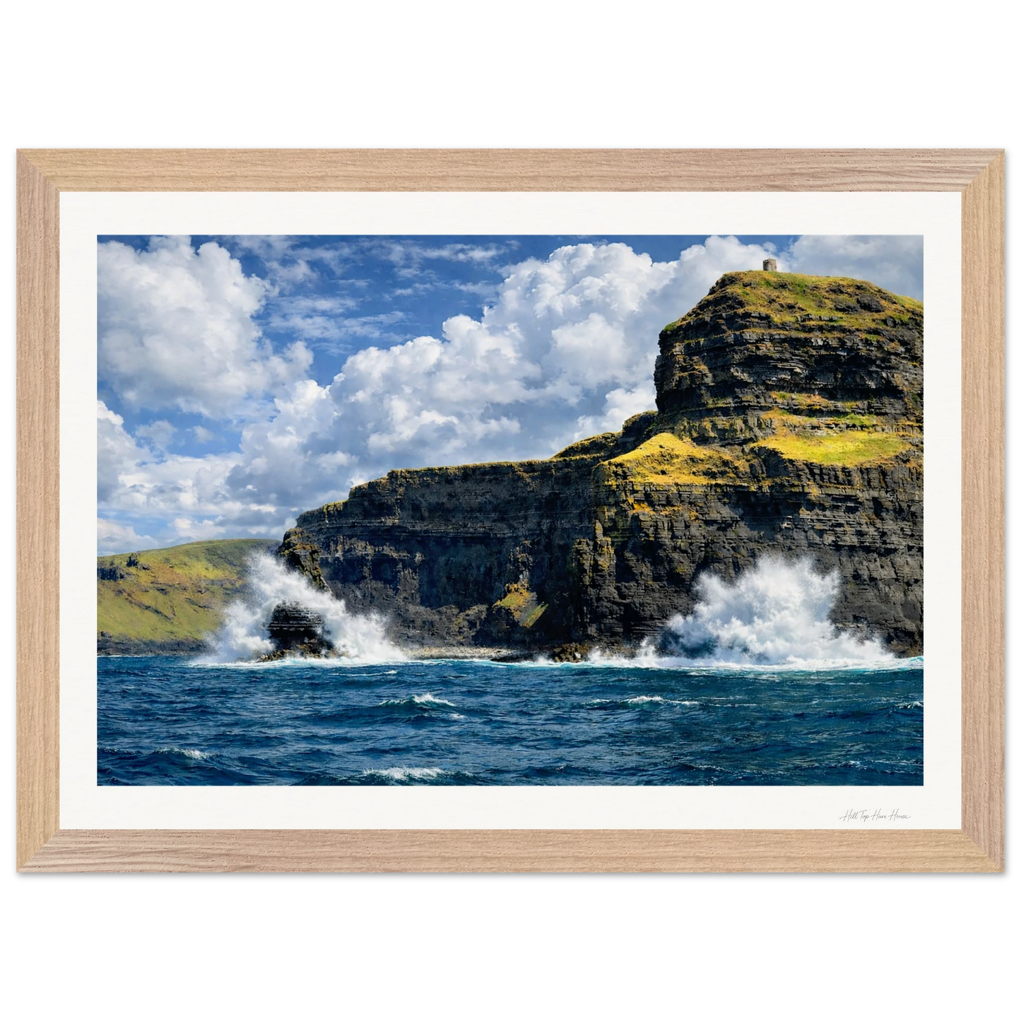 Framed photograph of a cliff with ocean waves crashing against it under a blue sky.