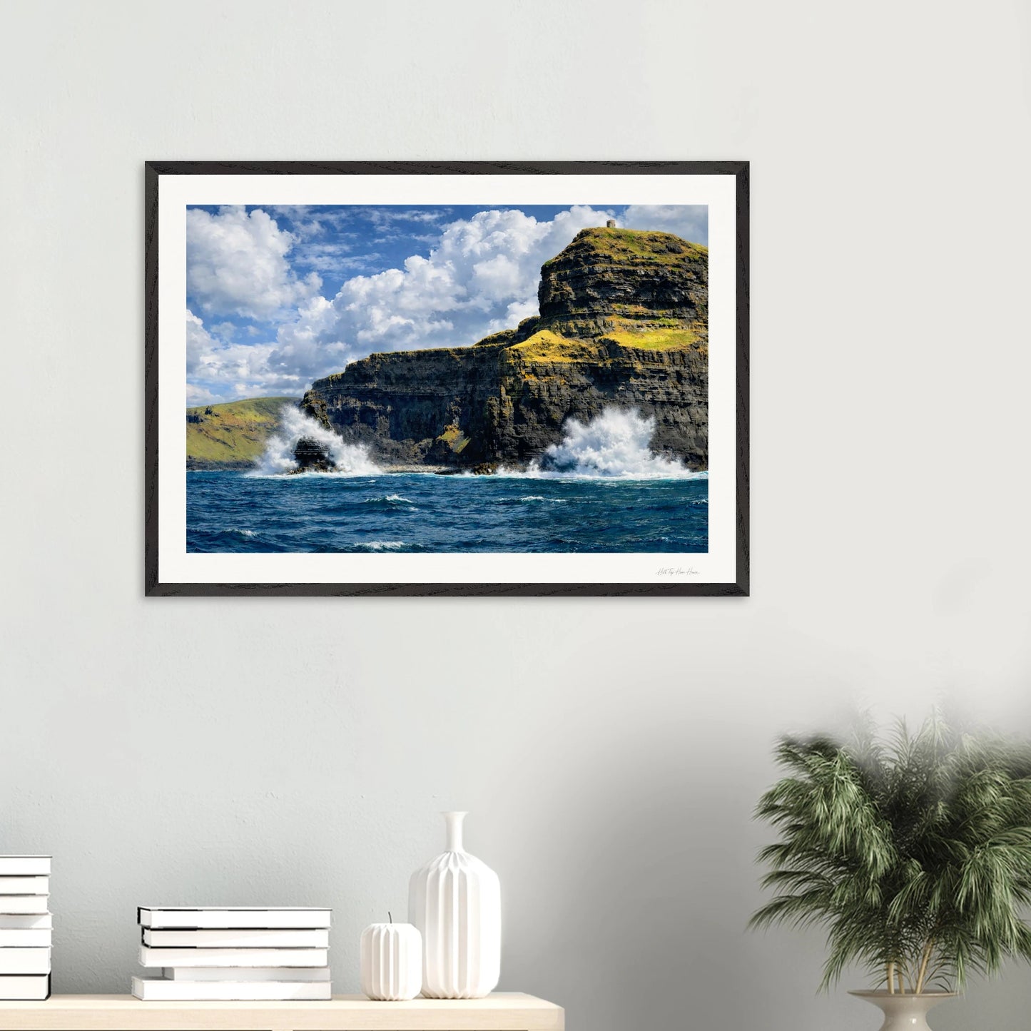 Framed artwork of a coastal scene with cliffs and ocean on a white wall.