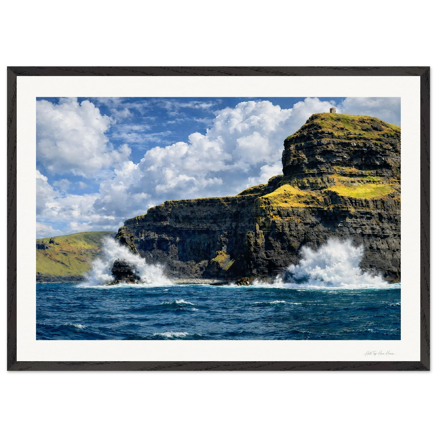 Framed photograph of a rocky cliff with ocean waves crashing against it under a blue sky.