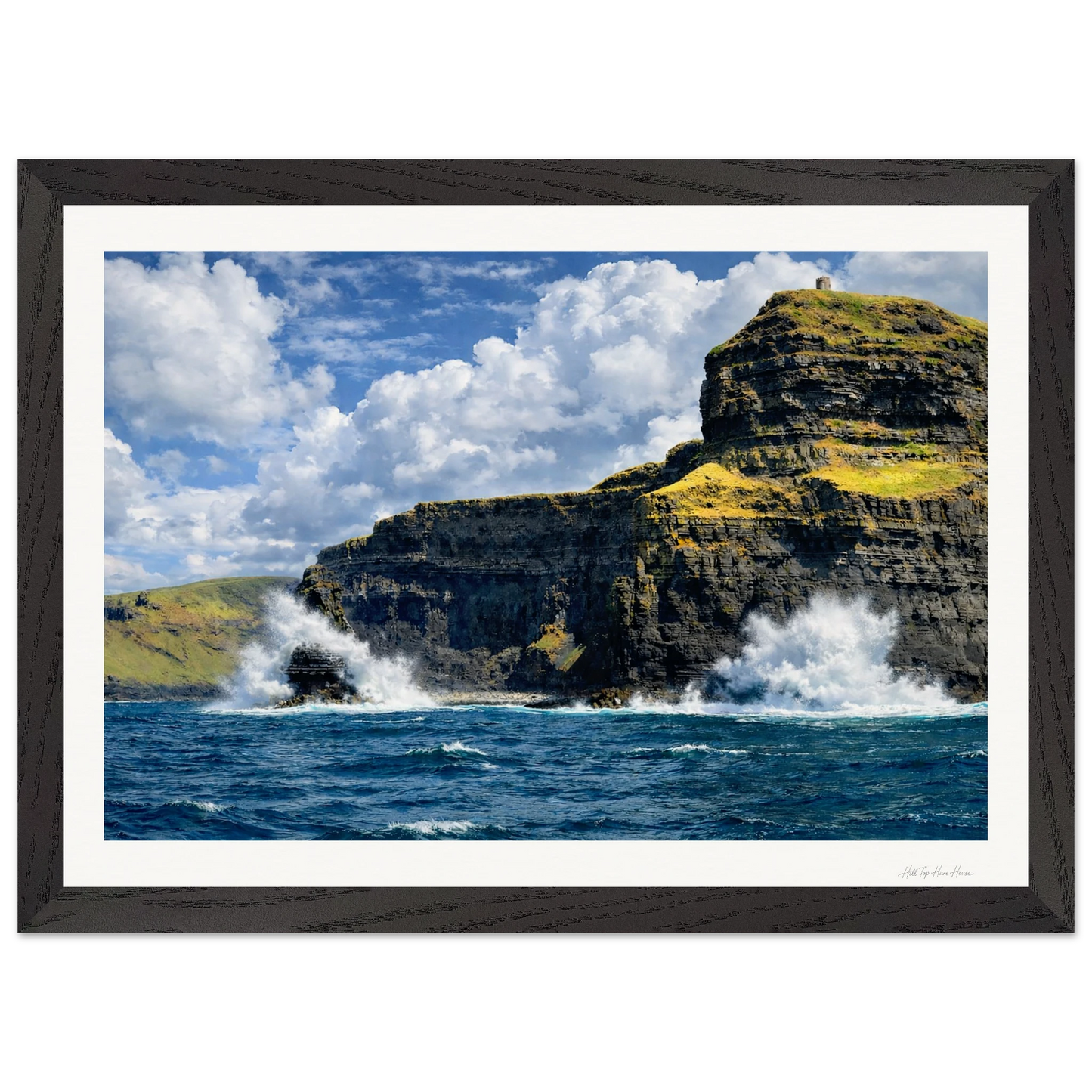 Framed photograph of a cliff with ocean waves crashing against it under a blue sky.
