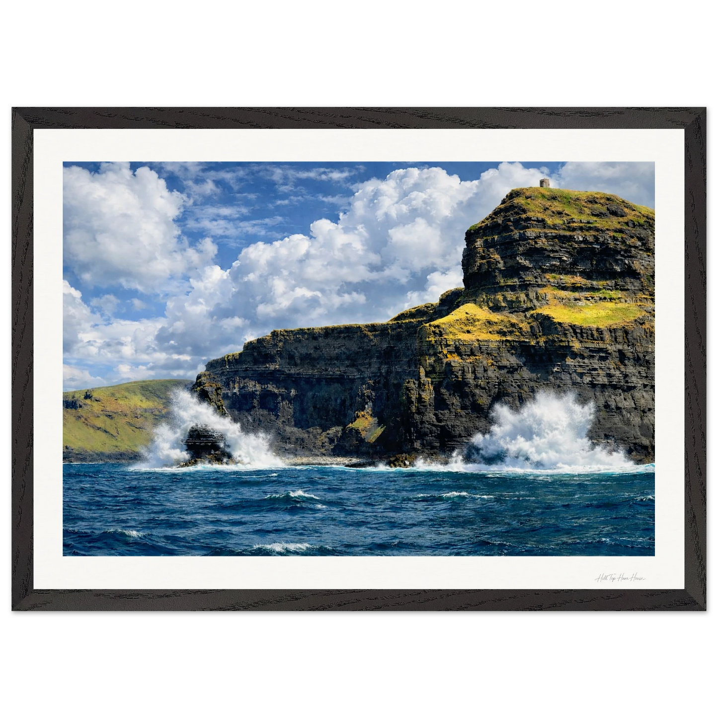 Framed photograph of a cliff with ocean waves crashing against it under a blue sky.