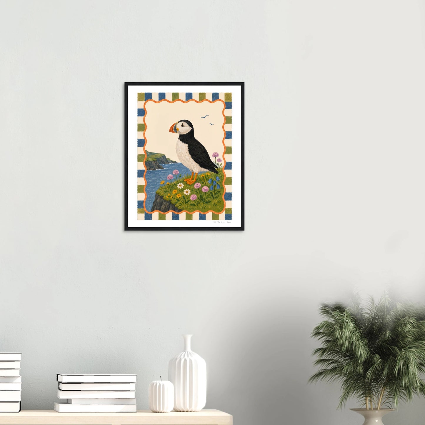 Framed artwork of a puffin on a striped background hanging on a wall.