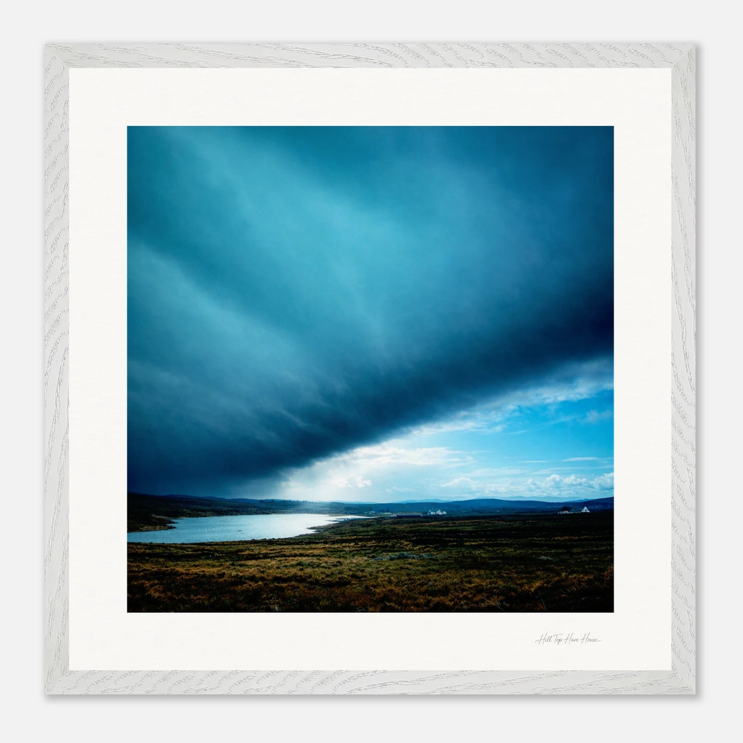 Framed artwork of a landscape with a blue sky and a body of water.