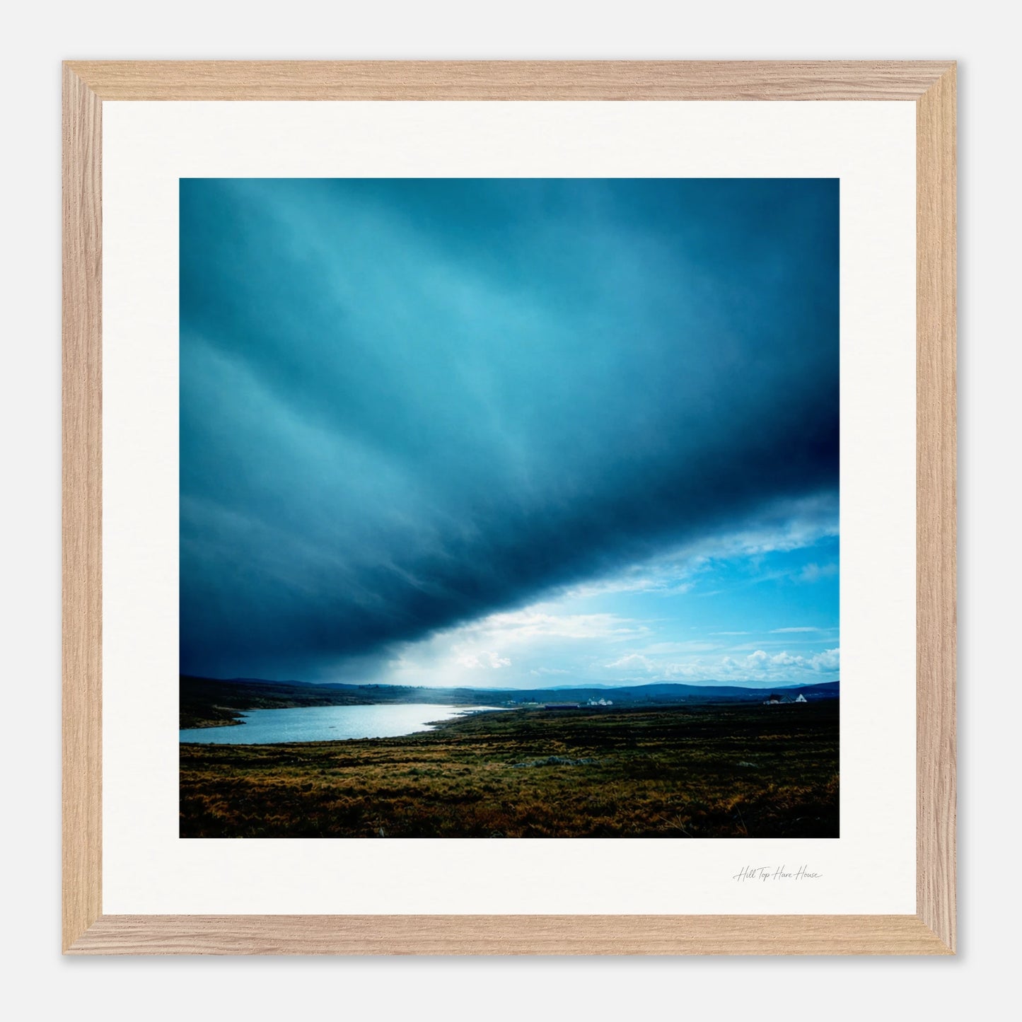 Framed artwork of a landscape with a blue sky and body of water.