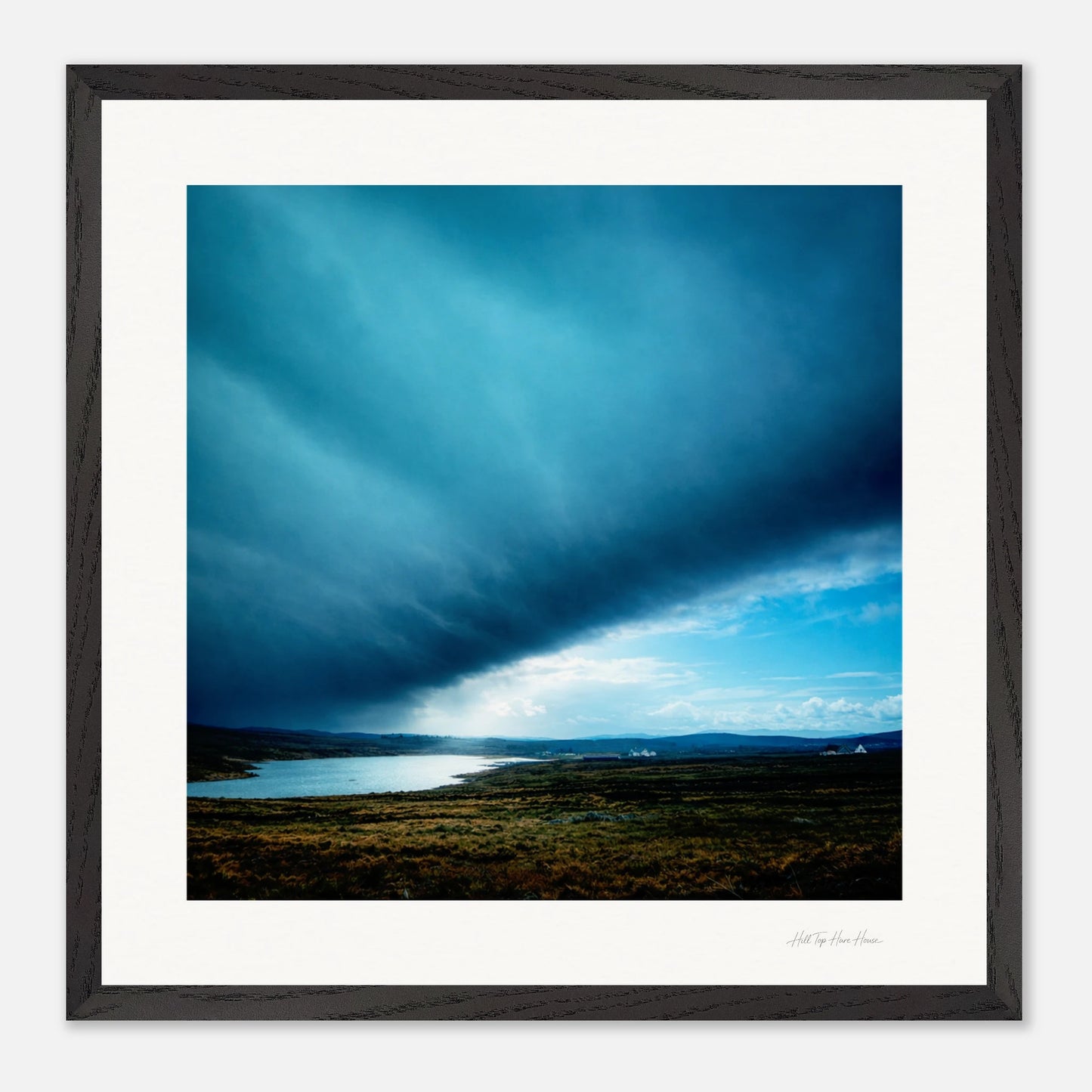 Framed artwork of a landscape with a blue sky and clouds over a body of water.