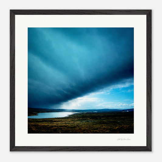 Framed artwork of a landscape with a blue sky and clouds over a body of water.