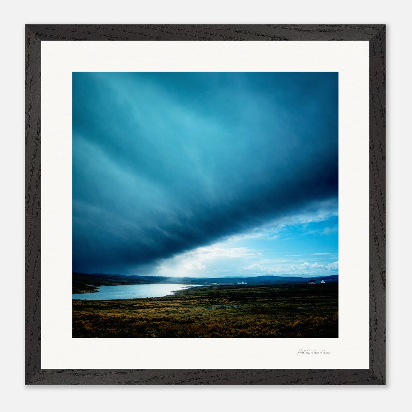 Framed artwork of a landscape with a blue sky and a body of water.