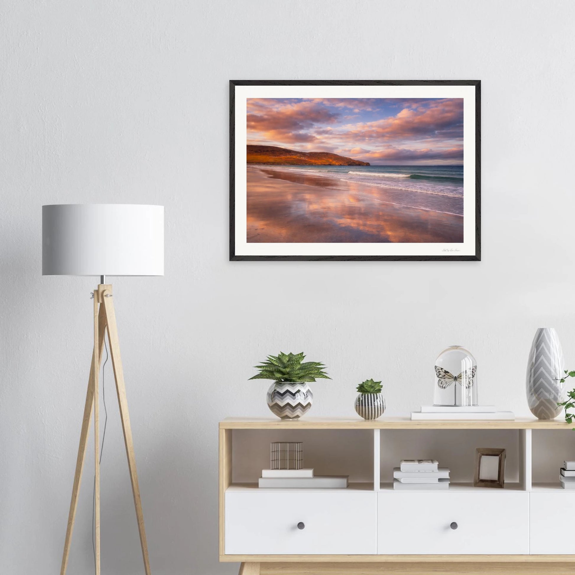 Framed artwork of a beach scene with a lamp and cabinet in the foreground