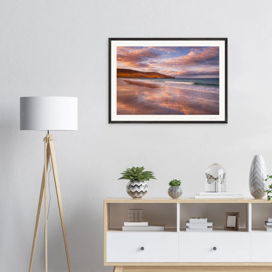 Framed artwork of a beach scene with a lamp and cabinet in the foreground