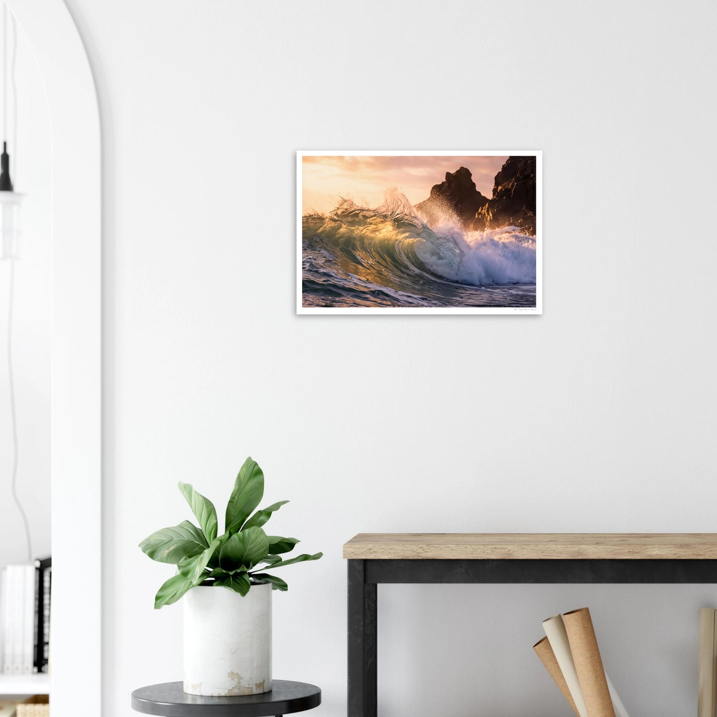 Framed artwork of a sunset over water with a plant and table in the foreground.