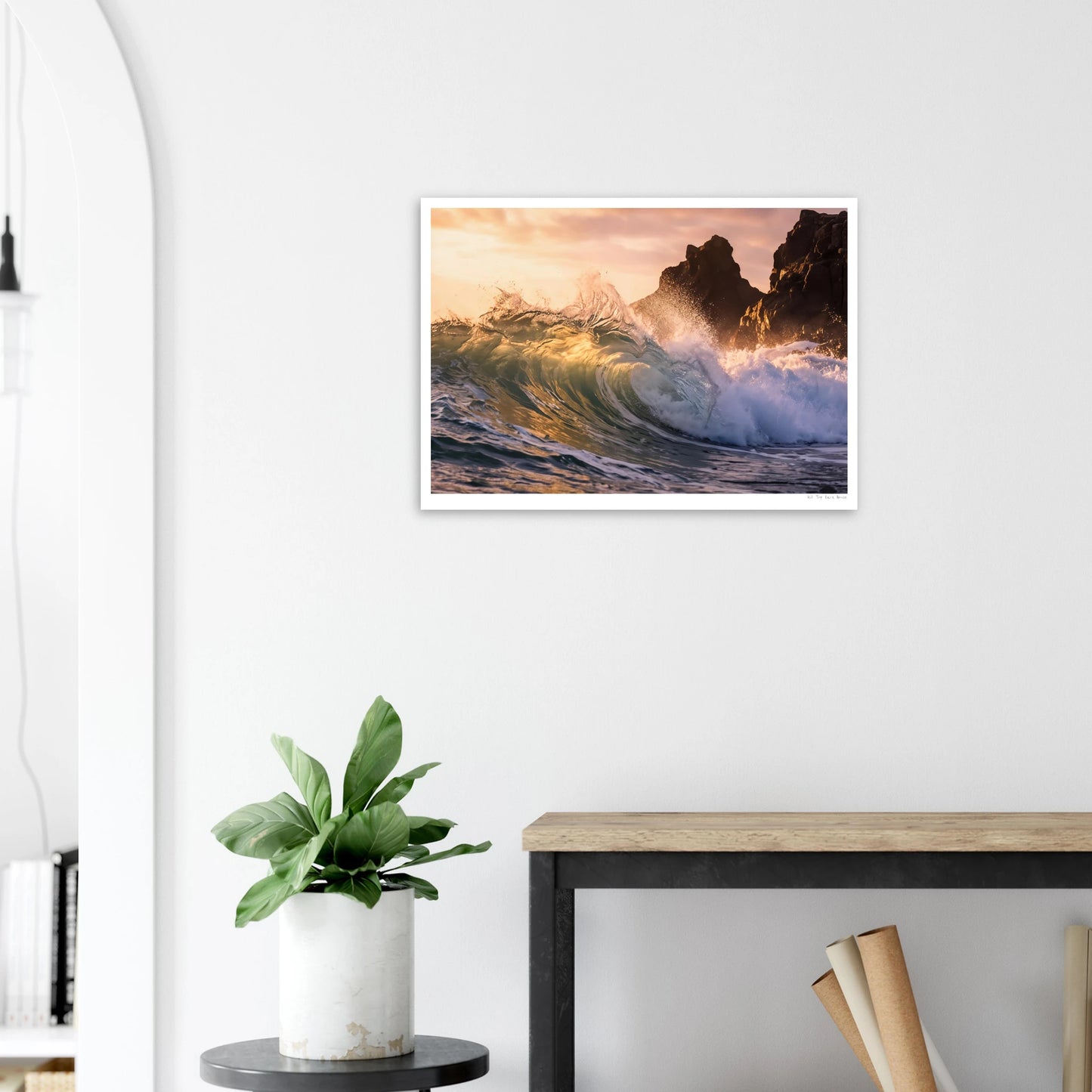 Framed artwork of a wave crashing against rocks on a wall above a desk with a plant.