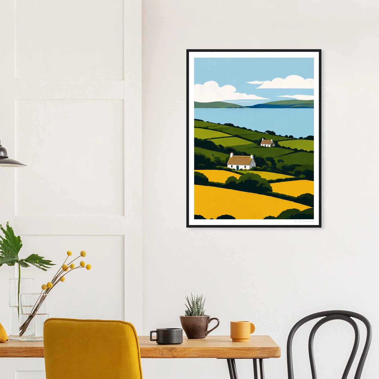 Framed artwork of a landscape with a house on a wall above a dining table.
