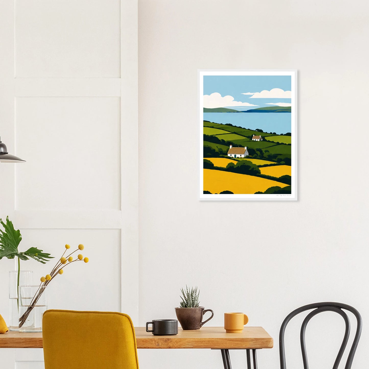 Framed artwork of a landscape with a house on a wall above a table with decor items.