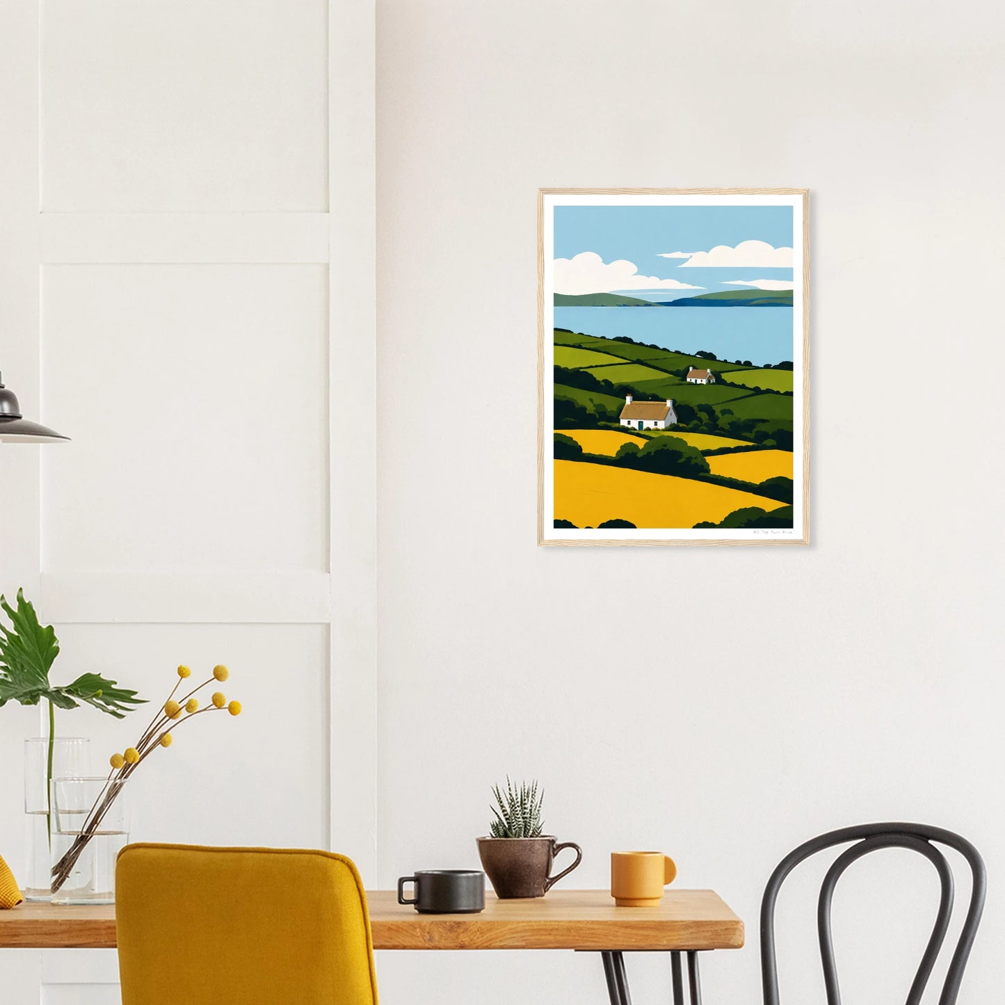Framed artwork of a landscape with a house on a wall above a dining table.