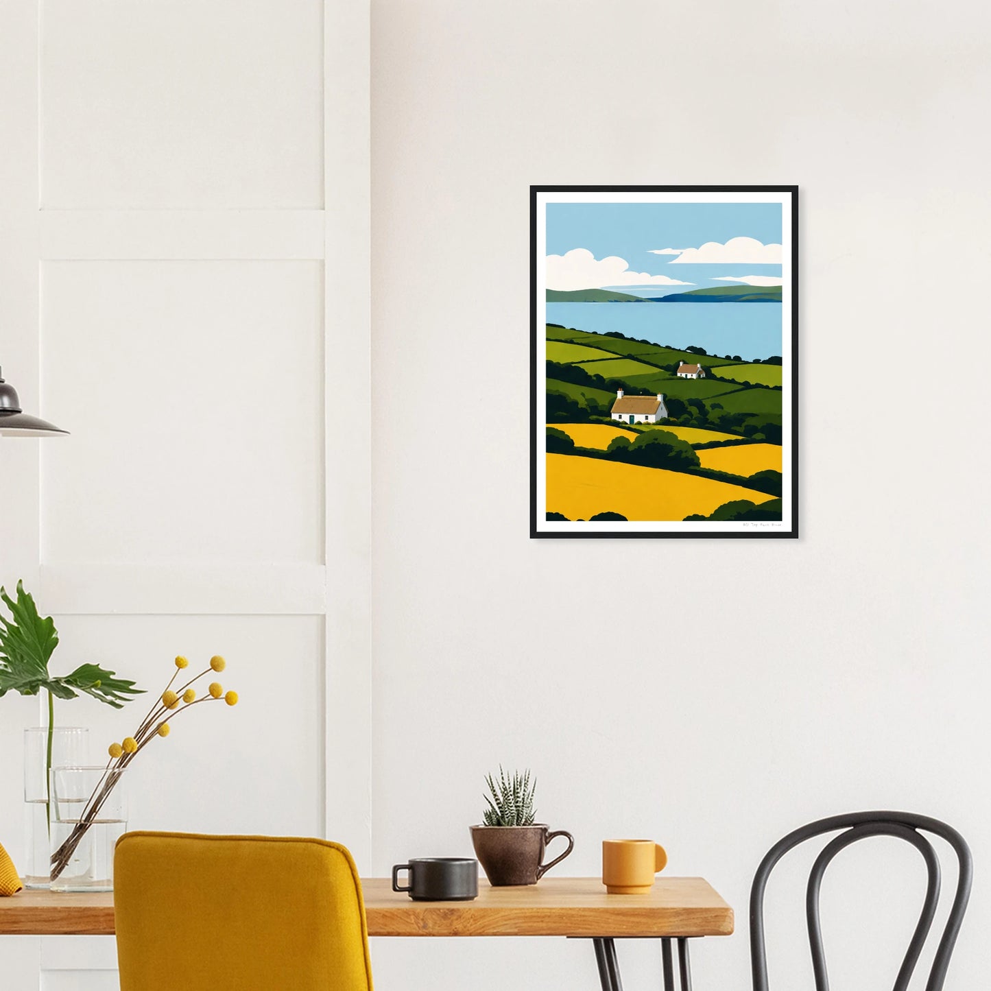 Framed artwork of a landscape with a house on a wall above a dining table.