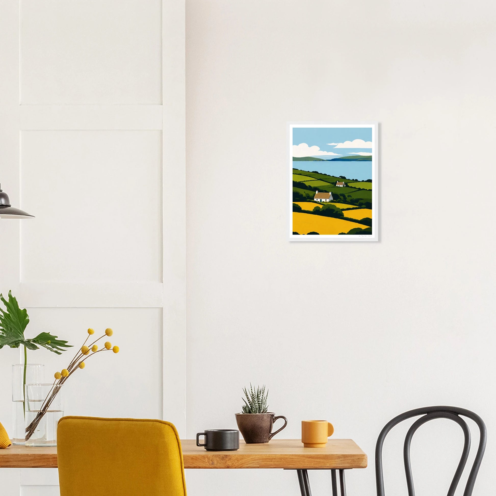 Framed artwork of a landscape hanging on a wall above a table with chairs.