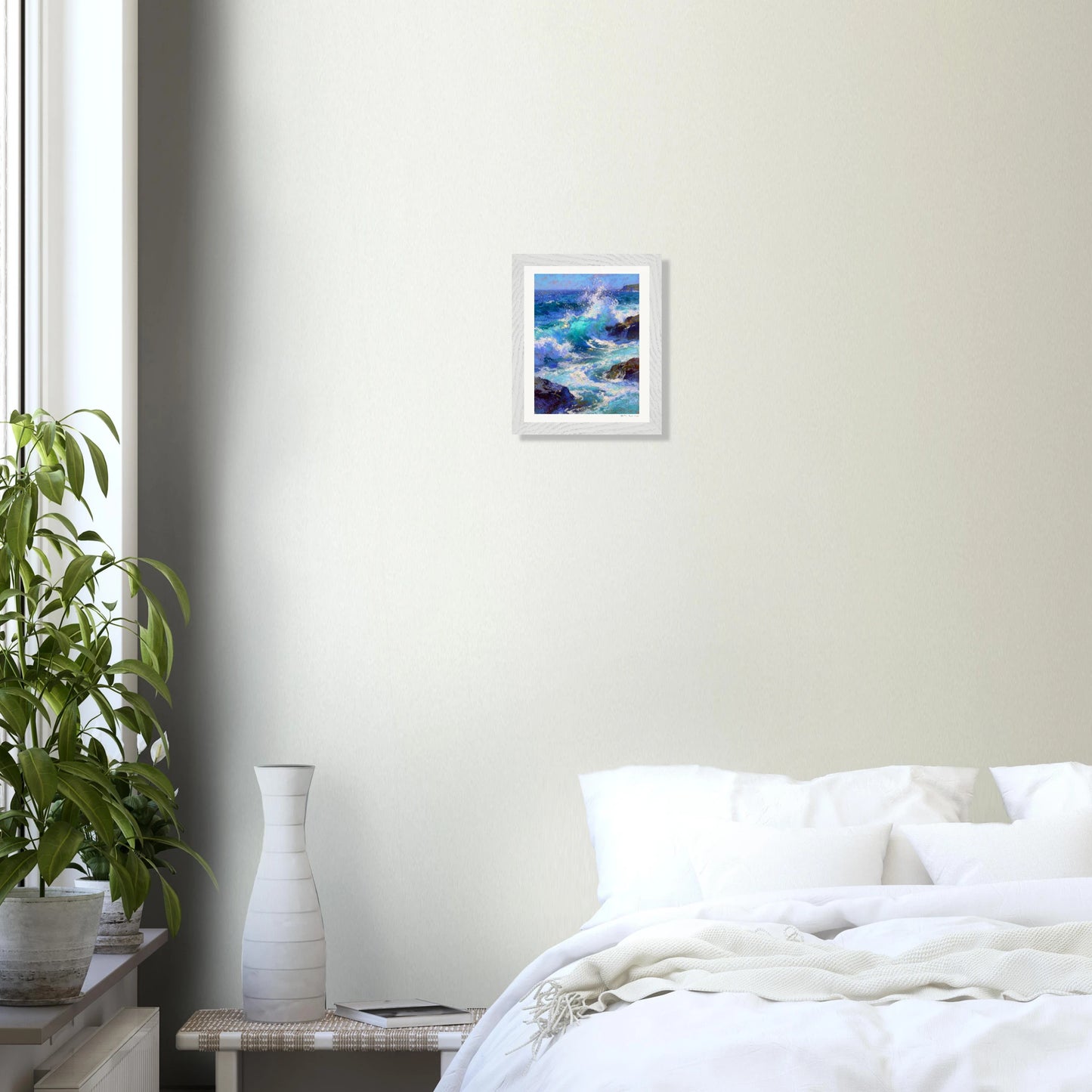 Framed artwork on a wall above a bed in a bedroom with a plant to the left.