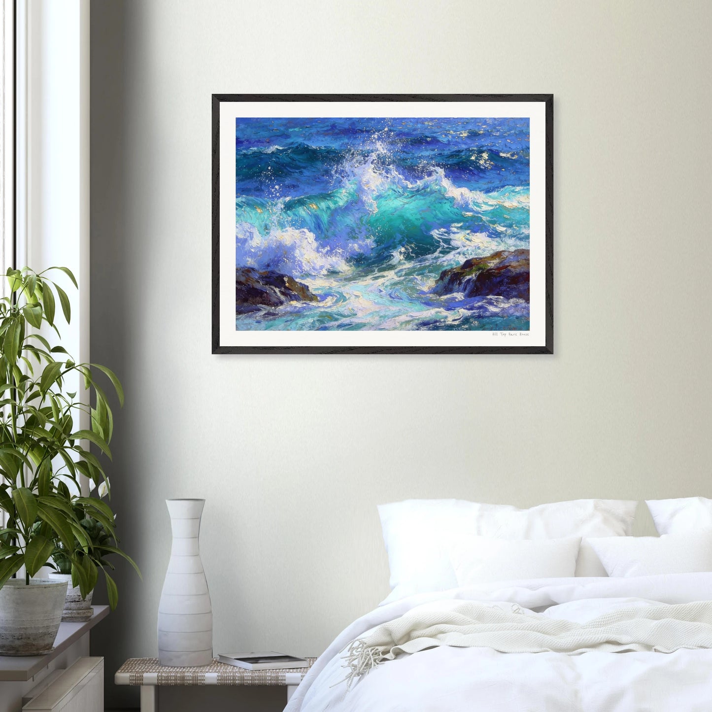 Framed painting of ocean waves on a wall above a bed