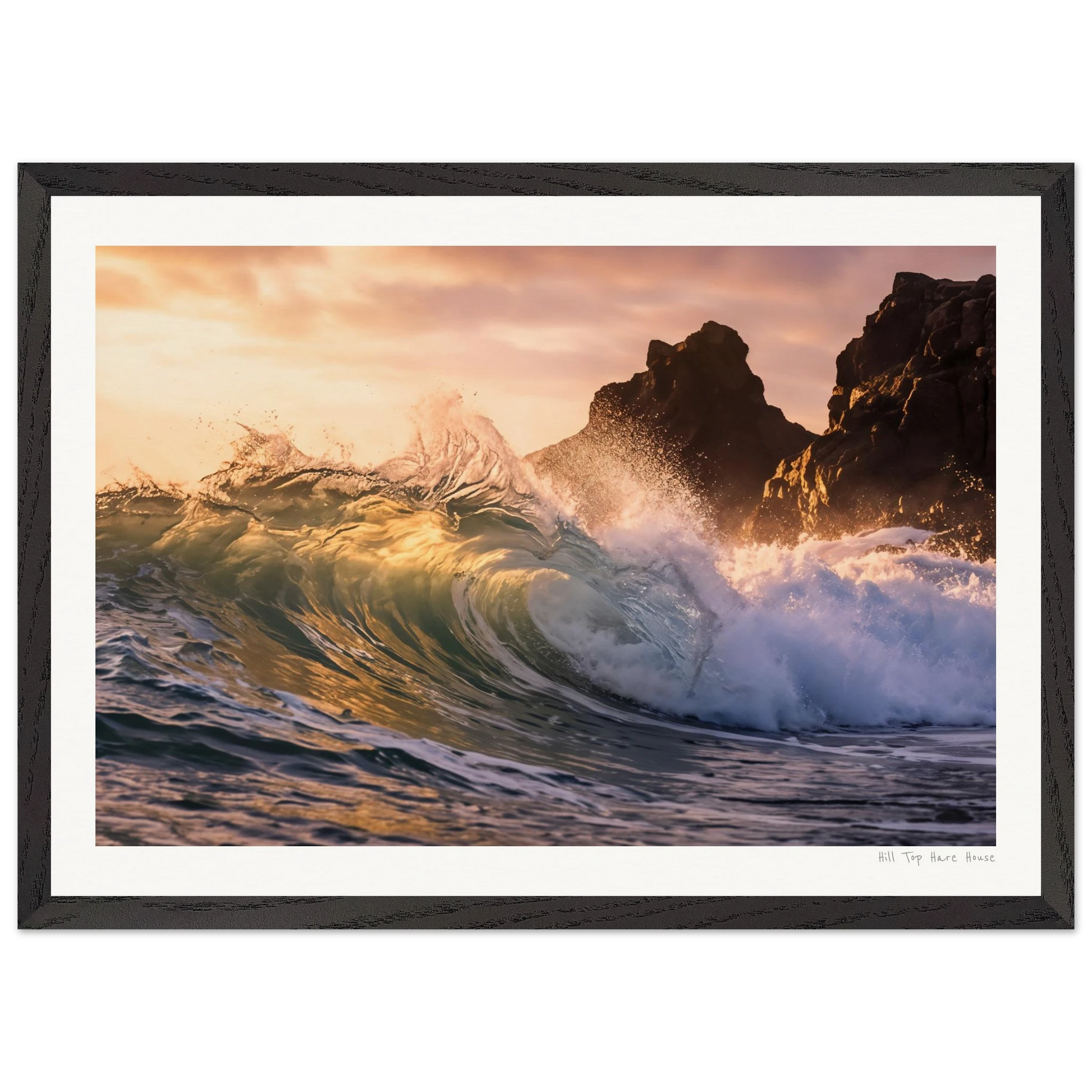 Framed photograph of a wave crashing against rocks at sunset.