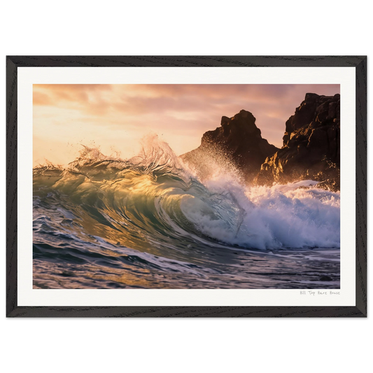 Framed photograph of a wave crashing against rocks at sunset.