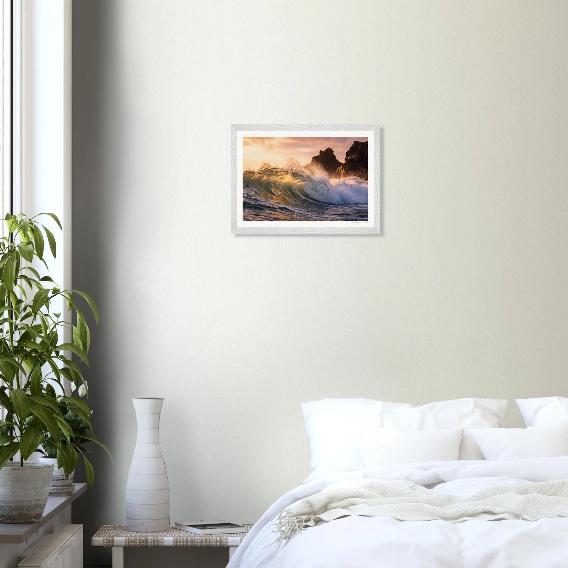 Framed artwork of a sunset over waves on a wall above a bed in a bedroom.