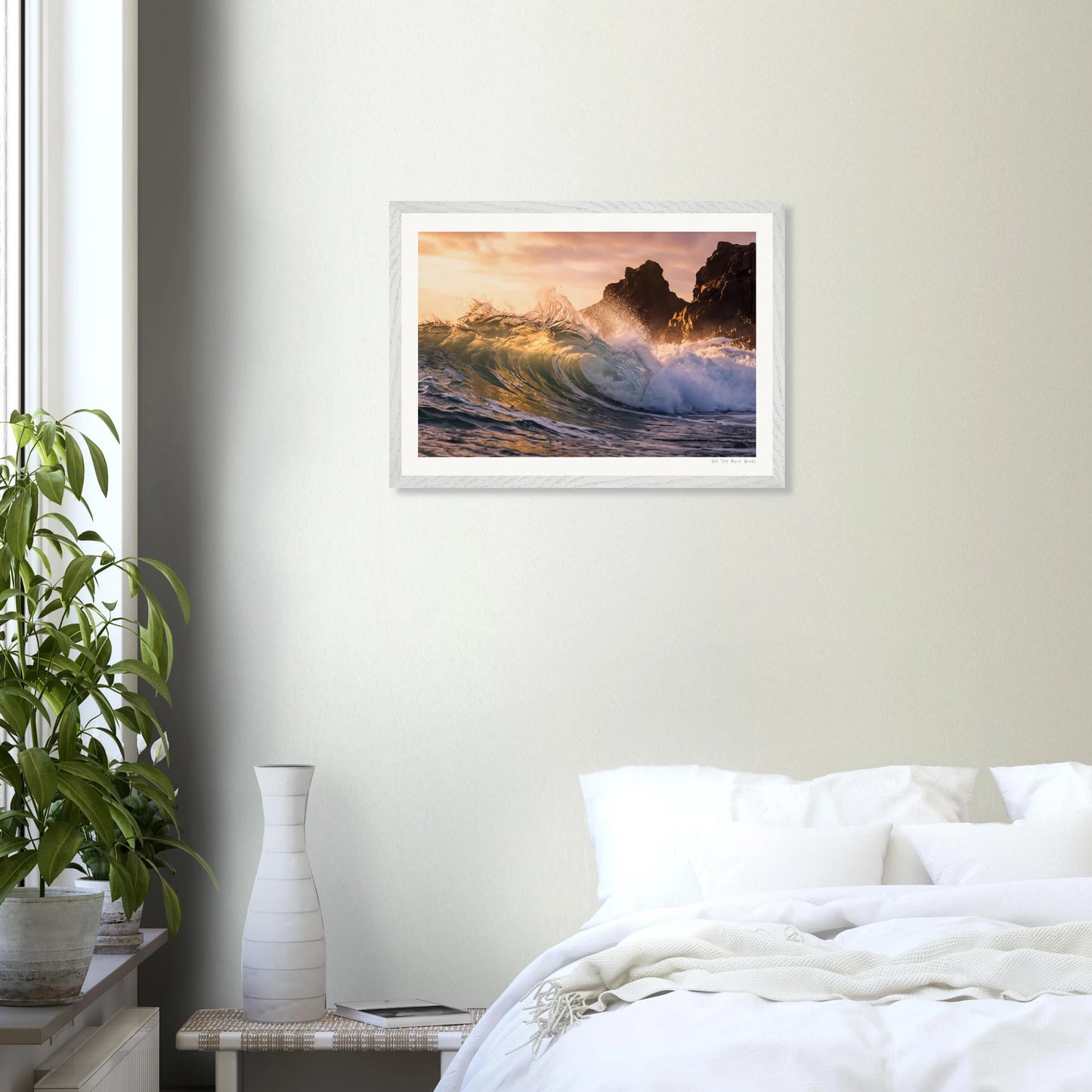 Framed artwork of a sunset over waves on a wall above a bed.